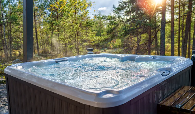 Hot tub with bubbling jets and rising steam against sunlit trees.