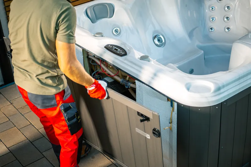 Technician repairing the control box and wiring in a hot tub side cabinet.