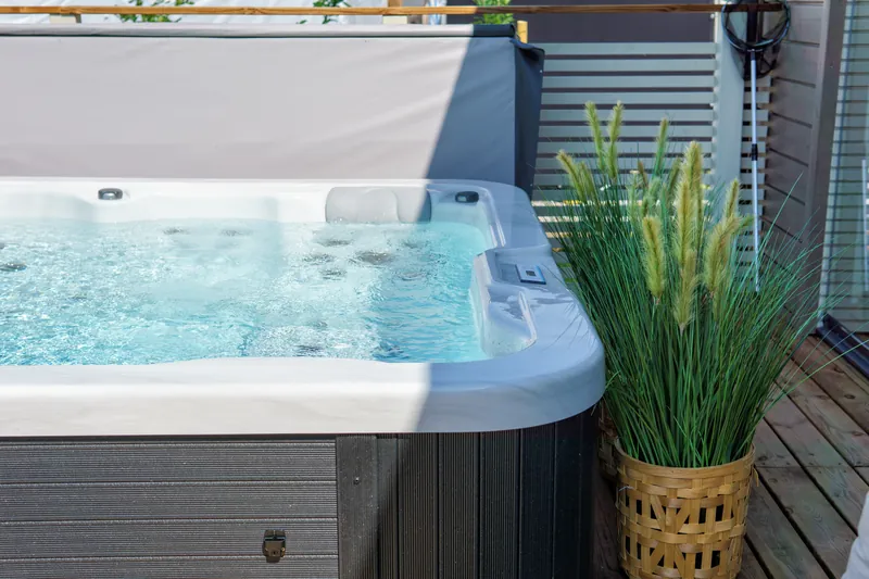 Corner of a modern dark-cabinet hot tub with clear water on a deck.